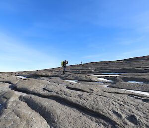 Five men are in an extended line searching a rocky hillside.