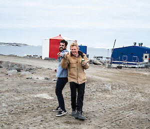 Two smiling men standing outside with the ocean visible in the background pose for the camera.