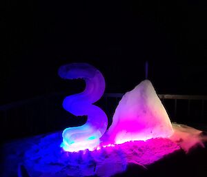 The number 3 and an iceberg like zero carved out of ice to make the number 30, are illuminated by bright pink and blue lights.