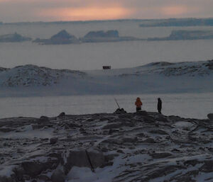 A grainy long distance shot shows two people on a hilltop.