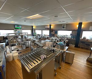 A very large hall with the entire contents of a commercial kitchen sitting on tables and benches around the room.