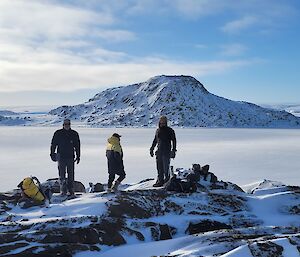 Three expeditioners stand overlooking the frozen ocean at Peterson Island, near Browning Peninsula.
