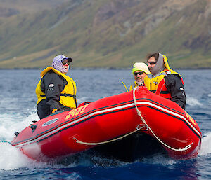 Red dinghy speeding along the water with three people in the boat and steep unwooded hills behind them