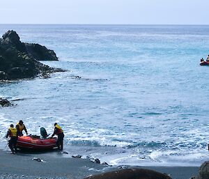 Red dinghy with three people standing next to it, being pulled up a beach