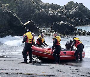 Four people in yellow life jackets pull a red dinghy up the beach