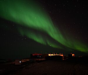 Green curtains of light over the top of buildings at night-time.