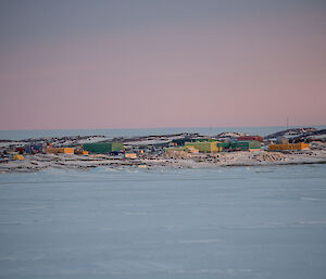 Many colourful buildings set in a snowy, rocky landscape with flat snow-covered sea-ice in the foreground.