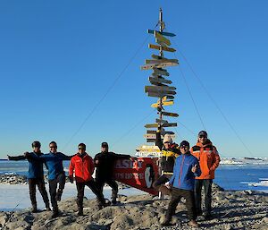 Six Chinese expeditioners posing for a photo beside the Casey Station sign on a clear day