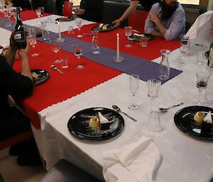 A beautifully presented dessert on black plates is shown on a large table with a number of people sitting and talking