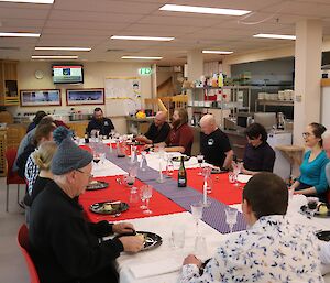 A number of people are saat around a large table with set with formal table cloths are cutlery. They are laughing and talking with each other while eating dessert.