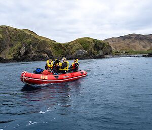 A red dinghy pulls up in an inlet with hills all around