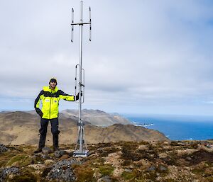 A man in yellow stands next to an antenna on a hillside