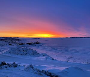 A vivid red and orange sunset with snow covered sea-ice in the foreground.
