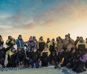 A group of people in two rows, wearing winter Antarctic clothing, ham it up for the photographer.