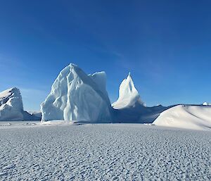Jagged and spire shaped icebergs on the sea-ice set against a vivid blue sky.
