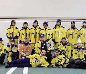 Fifteen smiling people in bright cold weather jackets and most in beanies pose for the camera