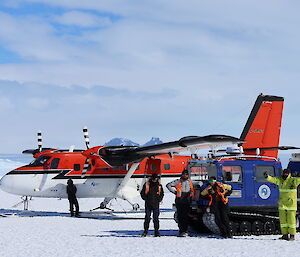 A man is refuelling a twin engined light aircraft while three men and a woman pose in front of a blue Hägglunds vehicle