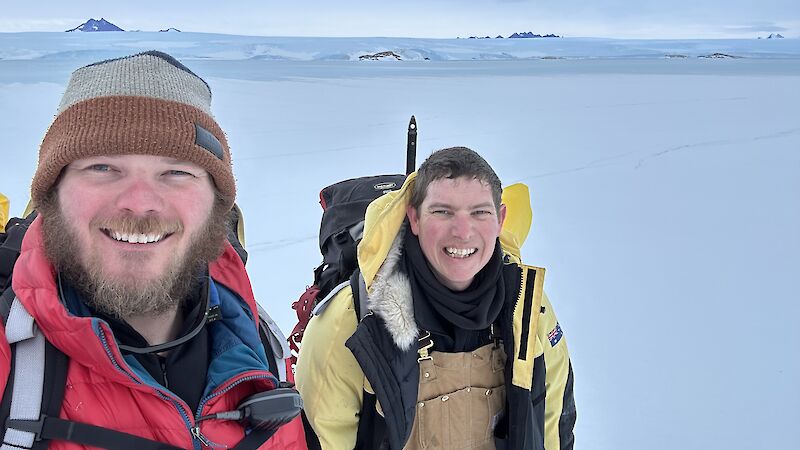 Two smiling dudes stand on an ice sheet