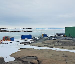A number of coloured buildings can be seen on a rocky landscape. There is an ice covered harbour in the background