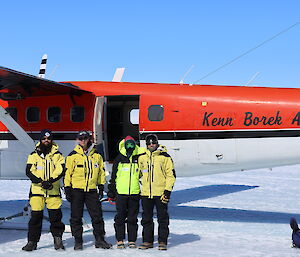 Two women and two men in bright yellow cold weather jackets are posing for a photograph in front of a light aircraft that is parked on the ice