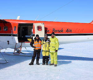 Three men are posing for a photograph in front of a light aircraft that is parked on the sea ice