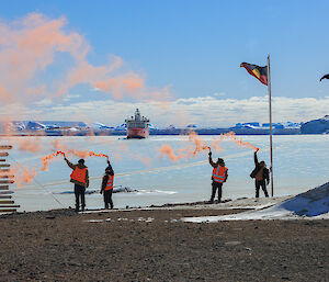 Four people hold flares above their head with RSV Nuyina in the background