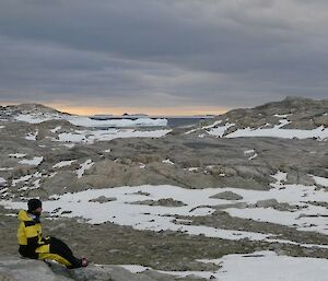 An expeditioner sitting on a rock looking out to the icebergs on the horizon