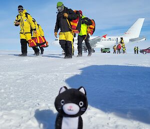 A stuffed cat toy on the snow with Antarctic expeditioners disembarking an Airbus A319 in the background
