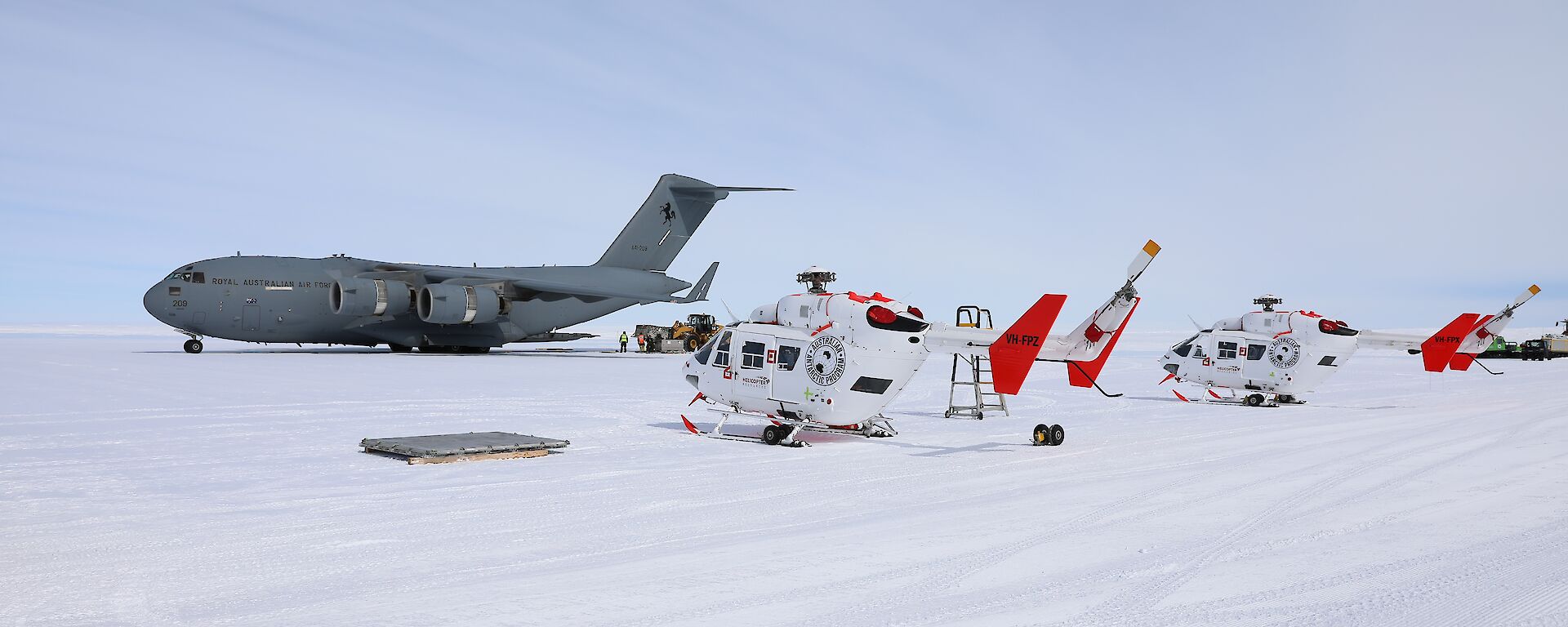 A C17 Globemaster sits on the ice with two helicopters in front of it.