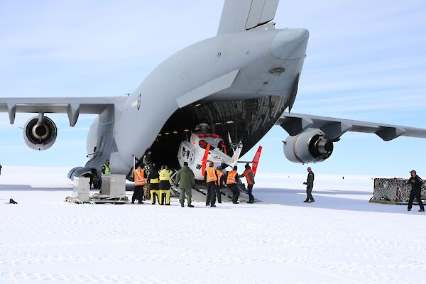 A helicopter being unloaded from the back of a large grey air force plane