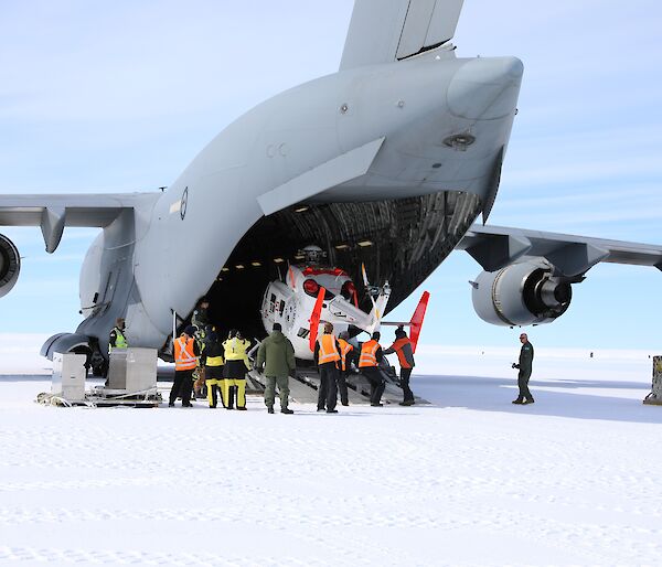 A helicopter being unloaded from the back of a large grey air force plane