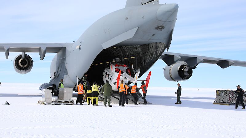 A helicopter being unloaded from the back of a large grey air force plane