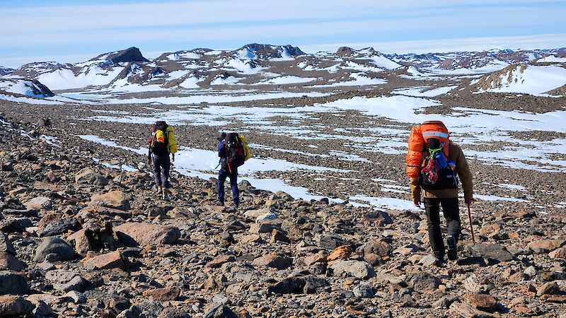 Three expeditioners walk across rocky and icy terrain at Bunger Hills