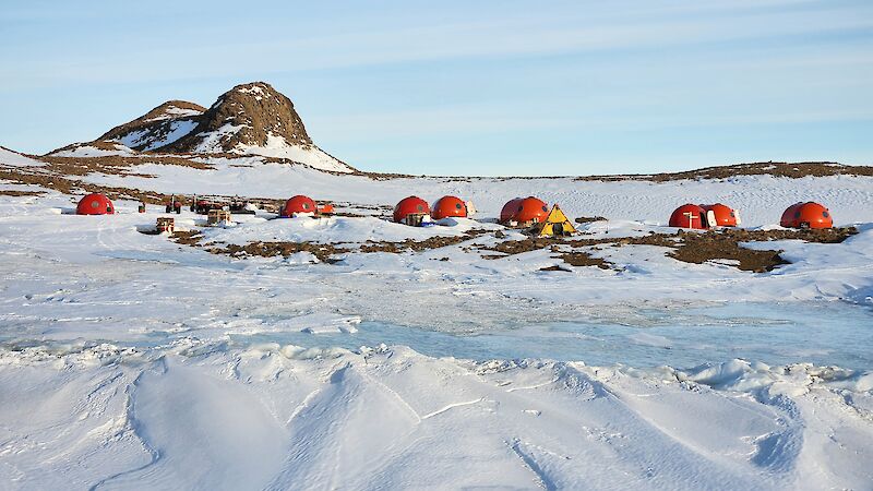Eight red melon tents on snow with rocky hills behind.