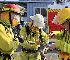 Three people in fire fighting uniforms prepare for a drill.