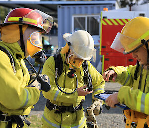 Three people in fire fighting uniforms prepare for a drill