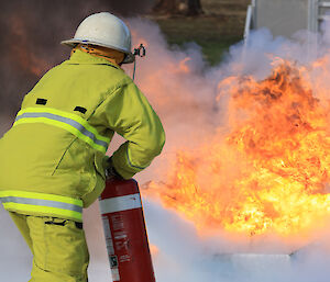 Expeditioner in fire fighting gear using a fire extinguisher on a large flame