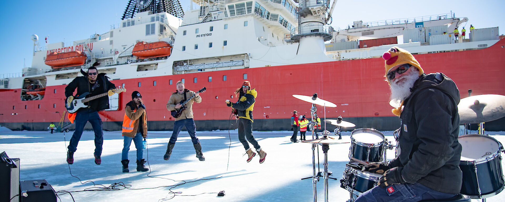 A band perform on the ice in front of a big red ship