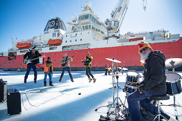A band perform on the ice in front of a big red ship
