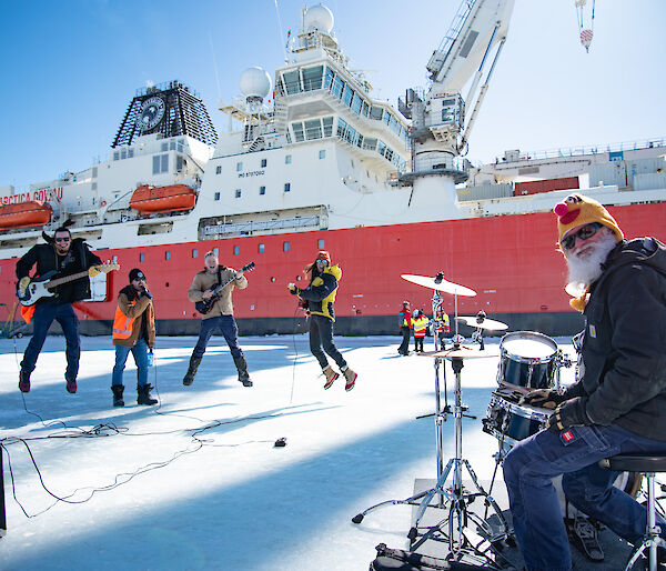 A band perform on the ice in front of a big red ship