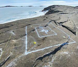 White paint markings on a rocky landscape depict a square hole to be cut. In the background is a frozen sea.