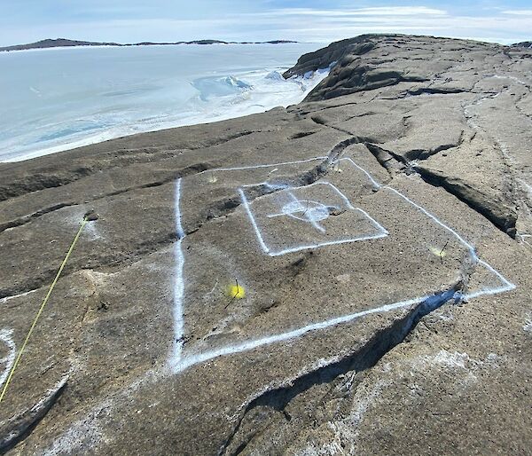 White paint markings on a rocky landscape depict a square hole to be cut. In the background is a frozen sea.