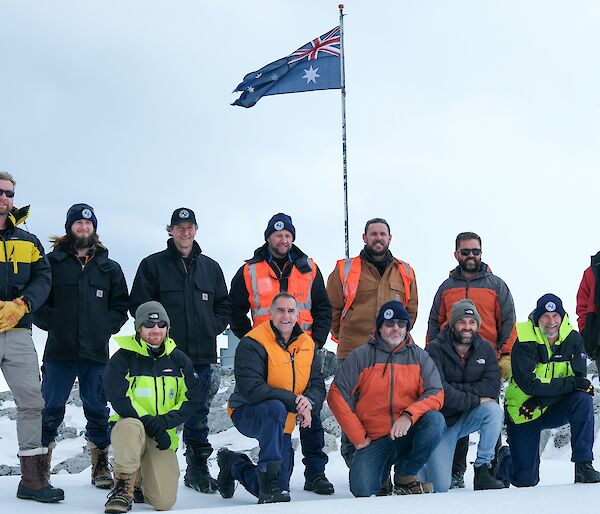 12 Expeditioners pose for a photo on the snow in front of the Australina, New Zealand and Canadian flags.