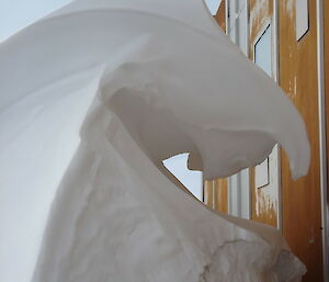 A frozen wave touches the side of a mustard-coloured metal building