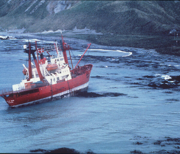 A red and white ship on rocks in a rocky bay.