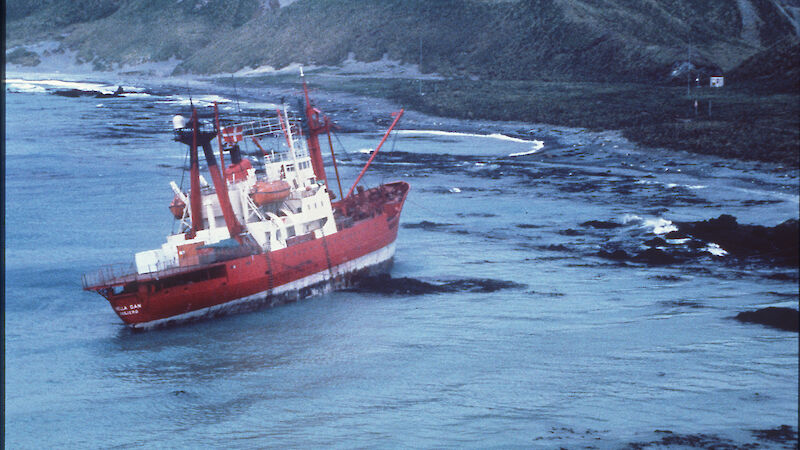 A red and white ship on rocks in a rocky bay.