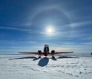 Front-on view of a Basler aircraft parked on snow with a sun halo in the sky above