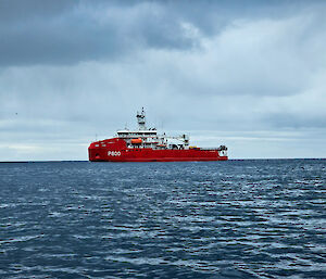 A red ship on a fairly flat blue sea with clouds above