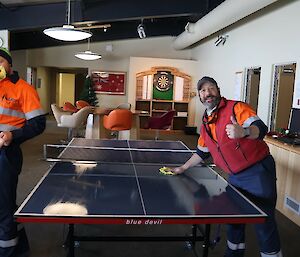 Two men standing either side of a table tennis table.