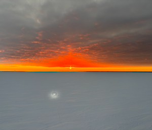 A red and orange glow from the sunset is visible in the far distance over a frozen sea